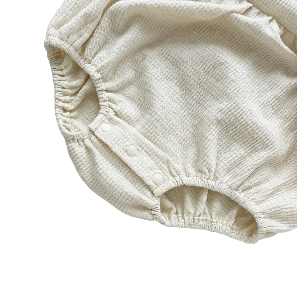 Secure bottom snap closures on the crotch of the cream waffle knit baby girl bubble romper.