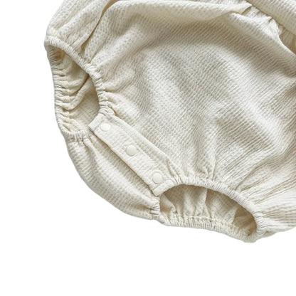 Secure bottom snap closures on the crotch of the cream waffle knit baby girl bubble romper.