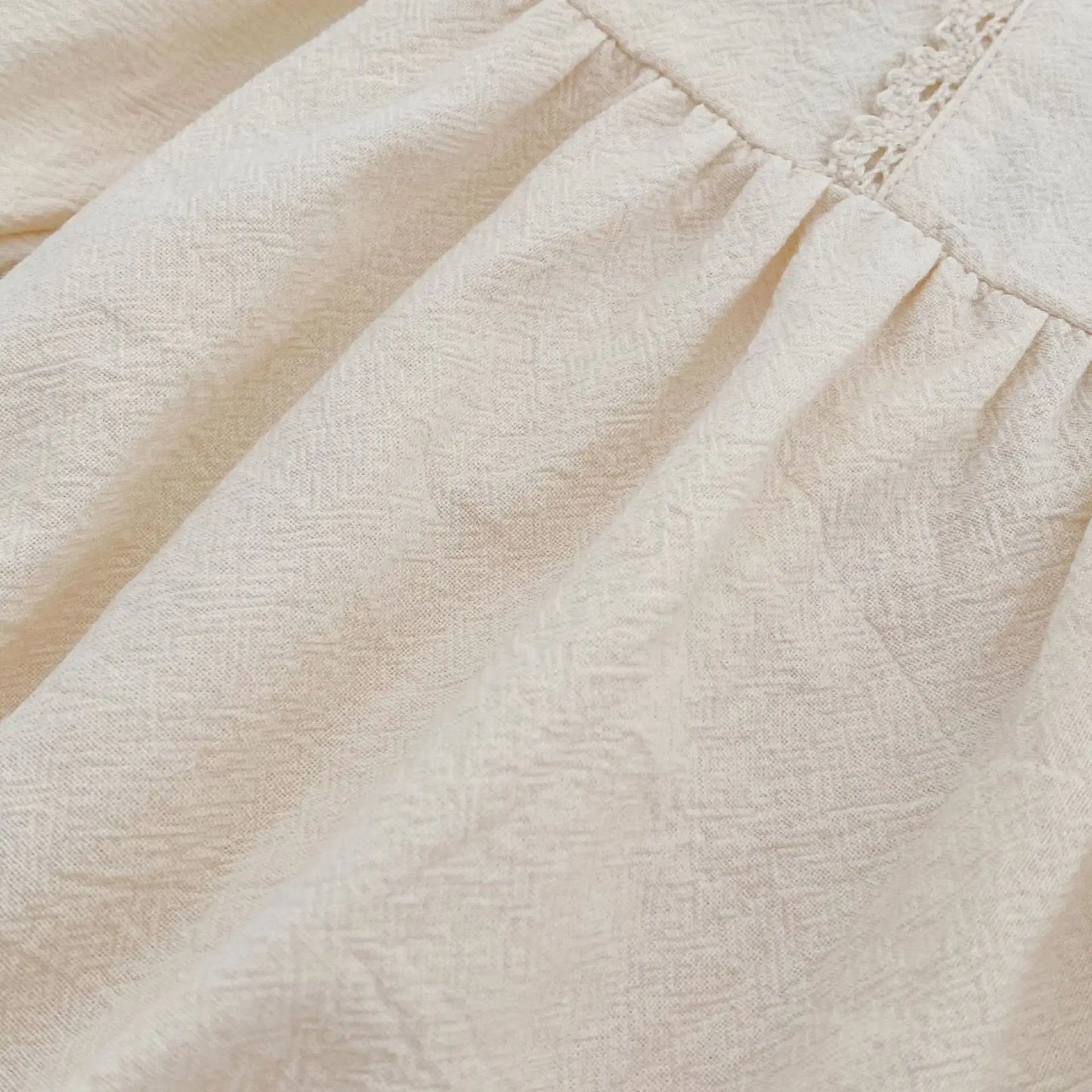 Close-up macro shot showing the soft, breathable woven cotton fabric texture of the cream baby girl bubble romper.