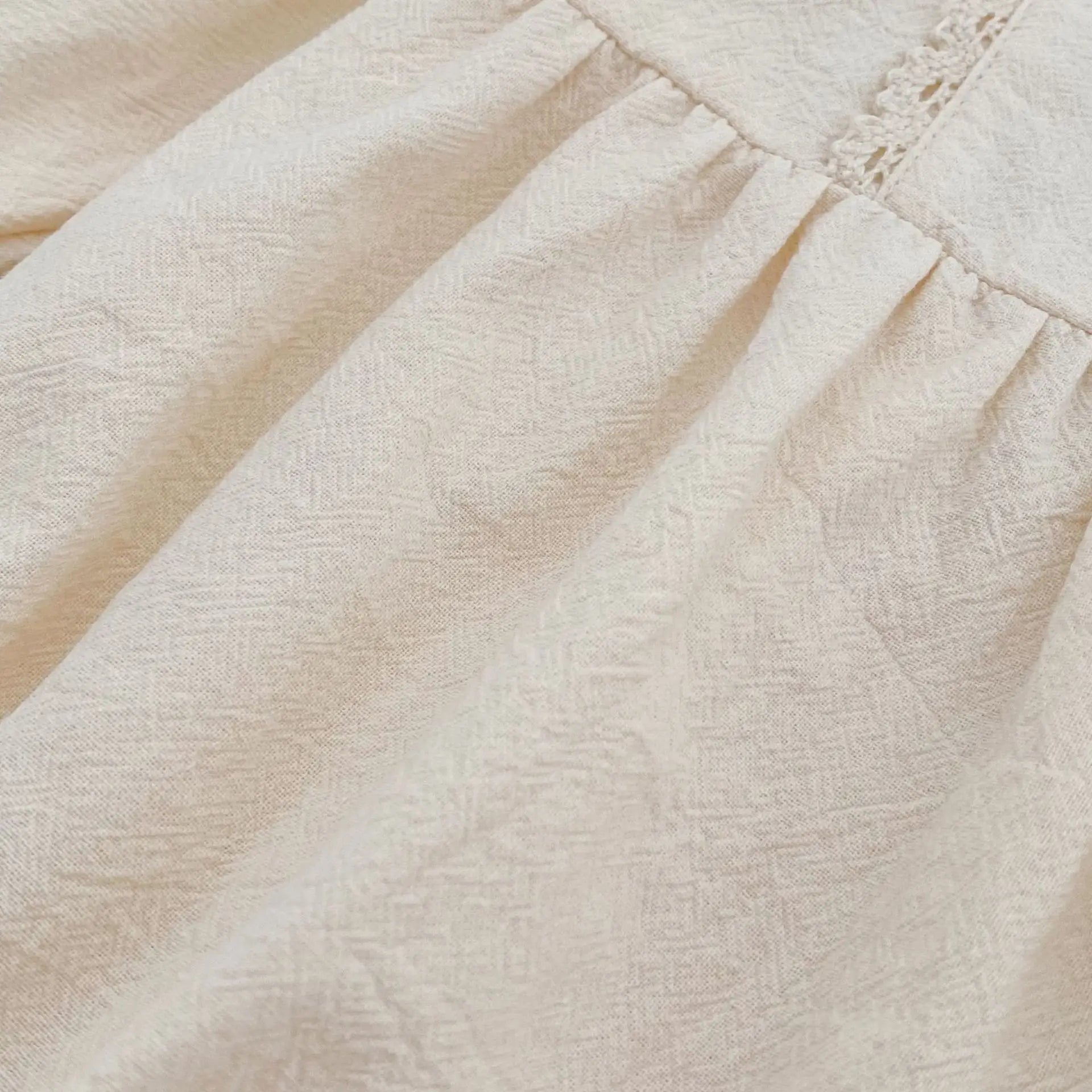 Close-up macro shot showing the soft, breathable woven cotton fabric texture of the cream baby girl bubble romper.