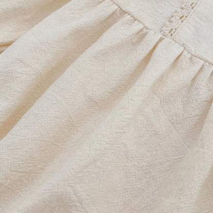 Close-up macro shot showing the soft, breathable woven cotton fabric texture of the cream baby girl bubble romper.