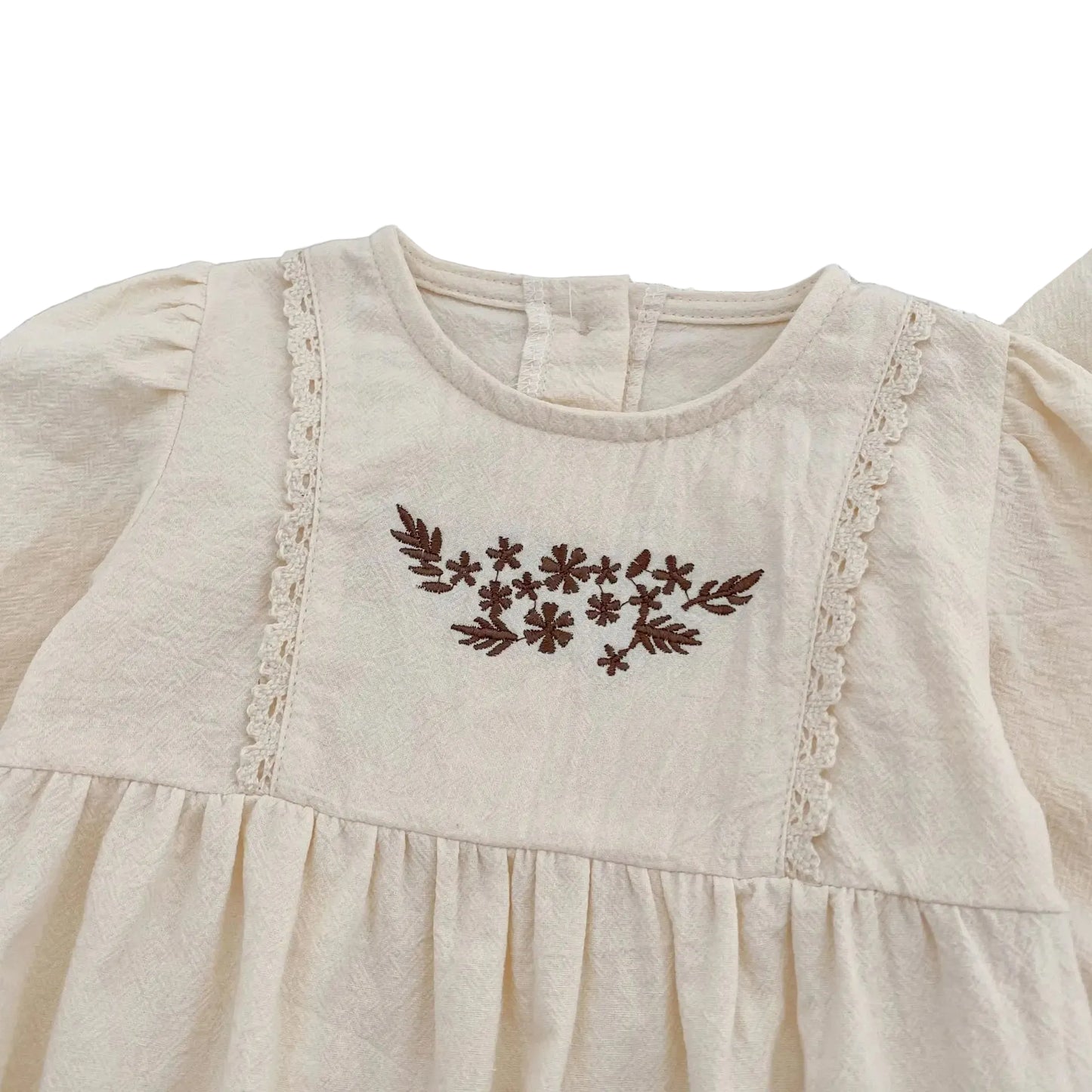 Close-up of the contrasting brown floral embroidery and vertical lace trim on the chest of the cream cotton baby girl bubble romper.