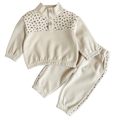 Baby and toddler girls cream sweatshirt and jogger set with a ditsy floral chest yoke and matching side stripes, laid flat on a white background.