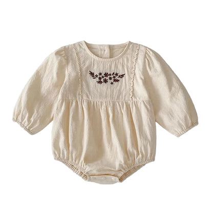 Front view of a vintage-inspired cream long sleeve baby girl bubble romper featuring brown floral embroidery and lace trim on the chest.