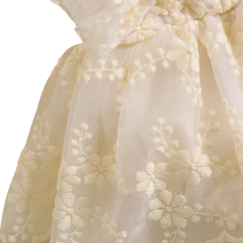 Close-up view of embroidered floral lace fabric and sheer overlay on baby romper dress
