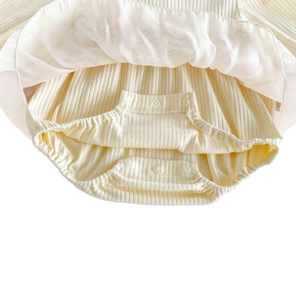 Underneath view of a baby girl's cream tulle romper showing the ribbed cotton blend material and convenient snap button closures at the bottom.