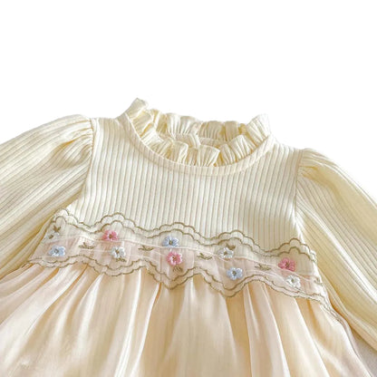 Close-up of the ruffled collar and pastel floral embroidery on the chest of a cream long-sleeve baby romper dress.