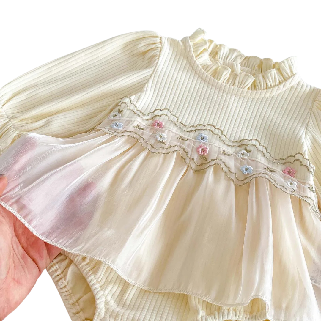Close-up detail of the pastel floral embroidery and layered cream tulle skirt overlay on a baby girl's romper.