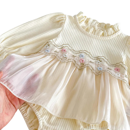 Close-up detail of the pastel floral embroidery and layered cream tulle skirt overlay on a baby girl's romper.