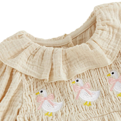 Close-up detail of the ruffled smocked neckline and sweet goose embroidery on the cream baby girl romper dress.