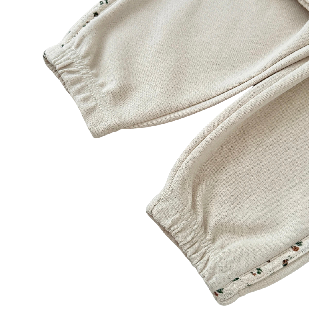 Close-up of the baby girls cream joggers showing the elastic ankle cuffs and the ditsy floral side stripe detail.