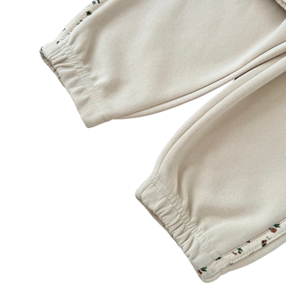 Close-up of the baby girls cream joggers showing the elastic ankle cuffs and the ditsy floral side stripe detail.