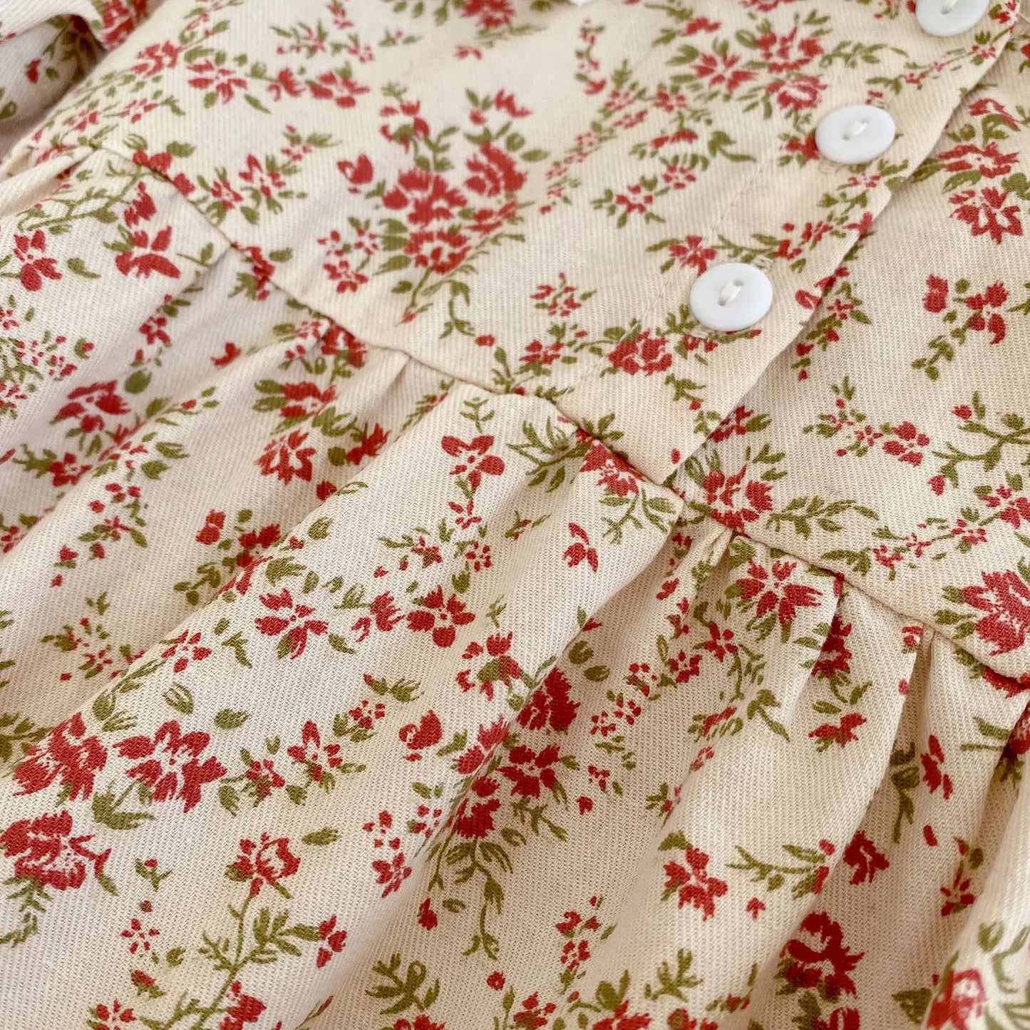 Close-up of the cream and red ditsy floral fabric and functional white front buttons on the baby girl vintage-inspired romper and dress.