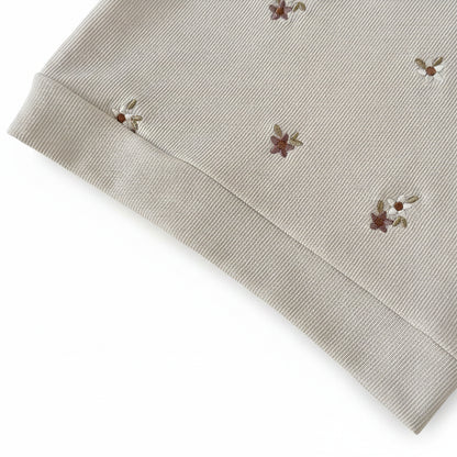 Close-up of the banded hem on a cream ribbed knit baby sweatshirt featuring earthy floral embroidery.