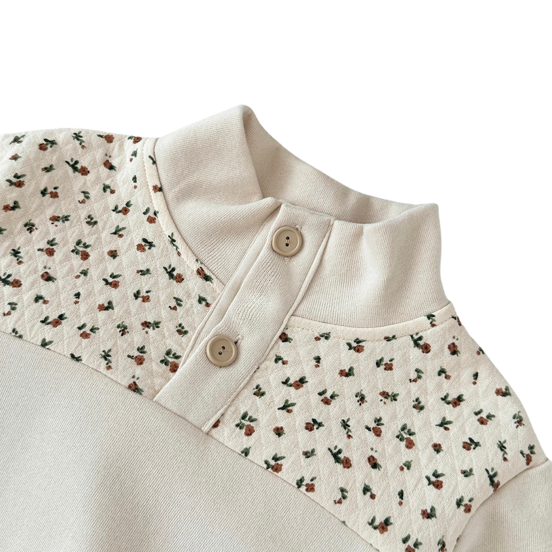 Close-up of the baby girls cream sweatshirt showing the quarter-button neckline and delicate ditsy floral print on the chest.