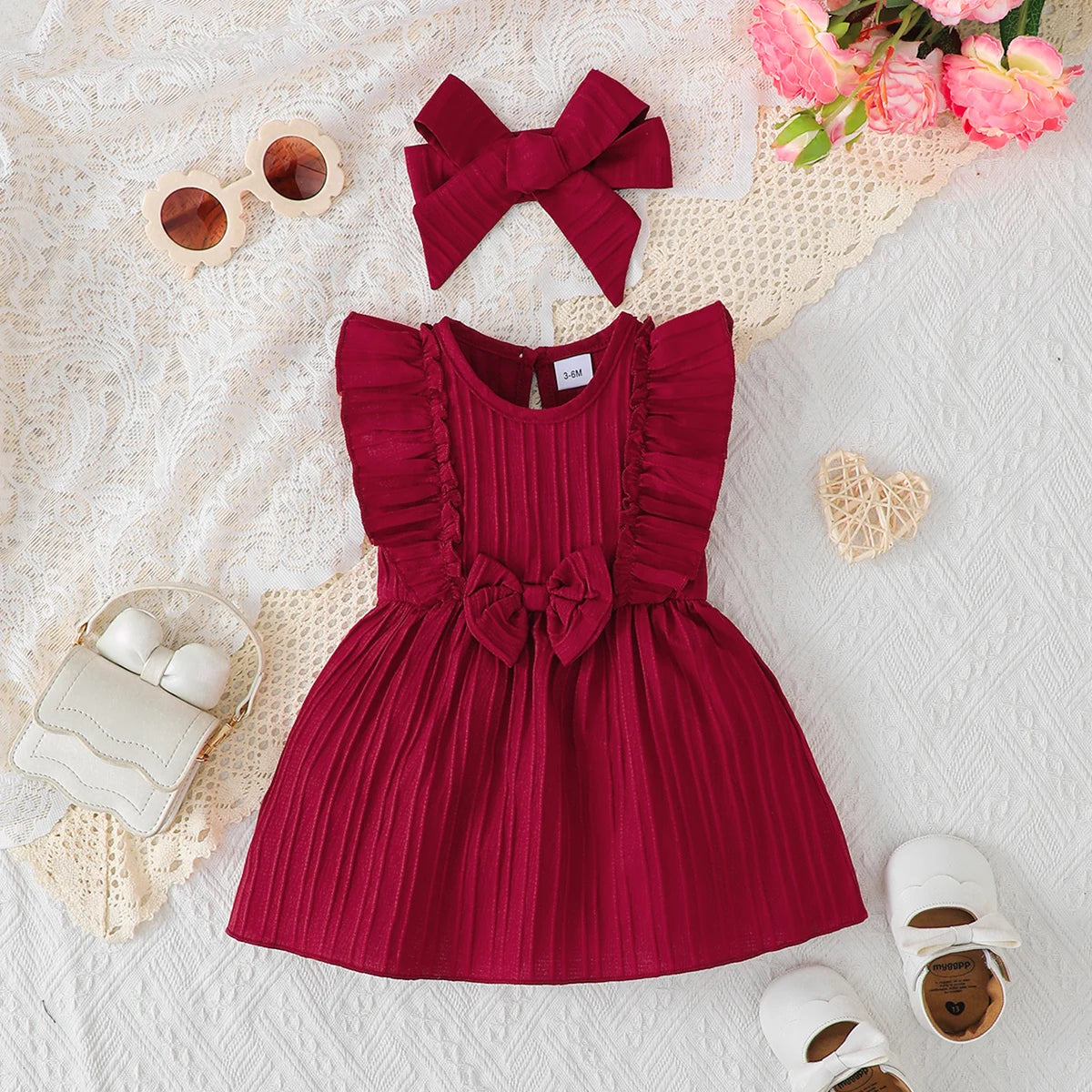 Flat lay display of the dark red baby girl summer dress and bow headband set, featuring ruffled shoulders and a textured weave.
