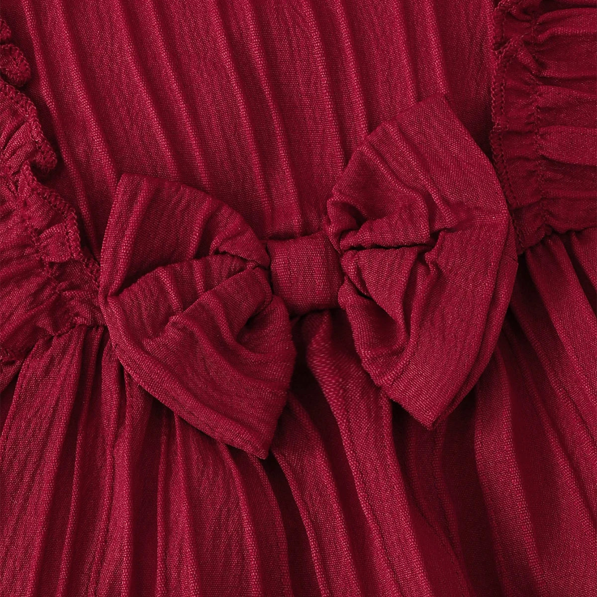 Close up detail of the center bow and breathable crinkled woven fabric on the dark red toddler sundress.