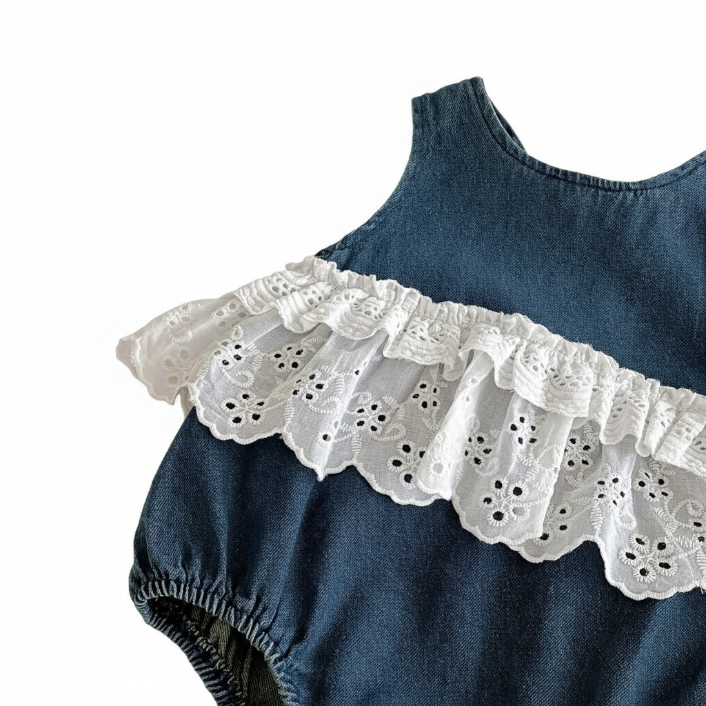 Close-up detail of the double-layered white cotton eyelet lace ruffles on a dark blue denim infant sunsuit.