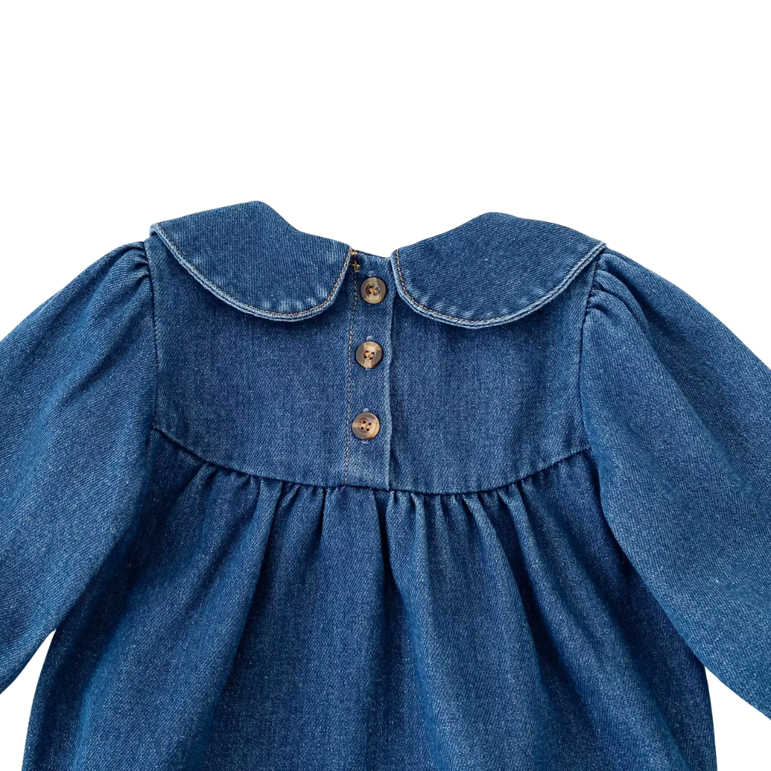 Back detail of dark blue denim baby romper showing button closures behind Peter Pan collar