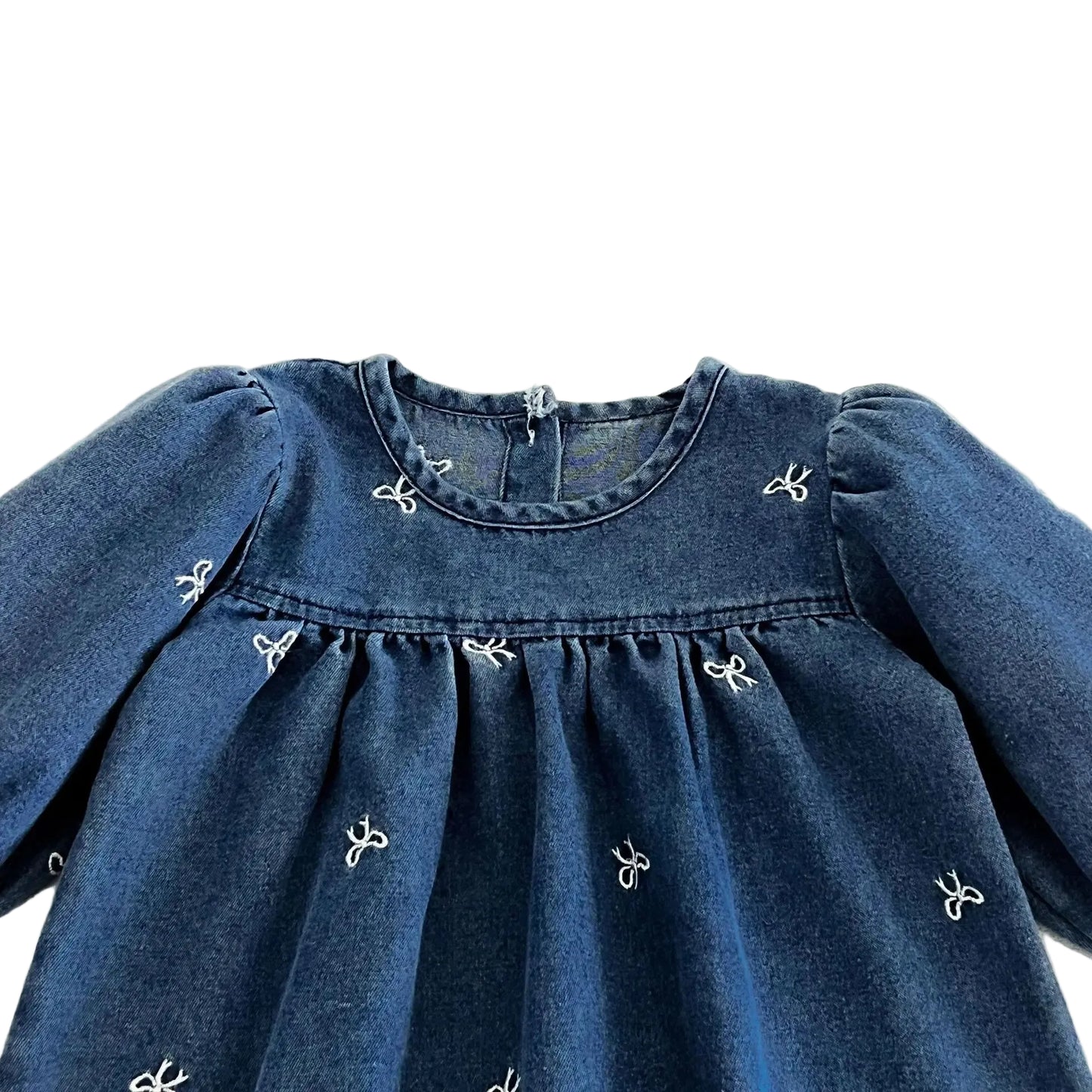 Close up of the gathered neckline and delicate white bow embroidery on the blue cotton denim baby dress.