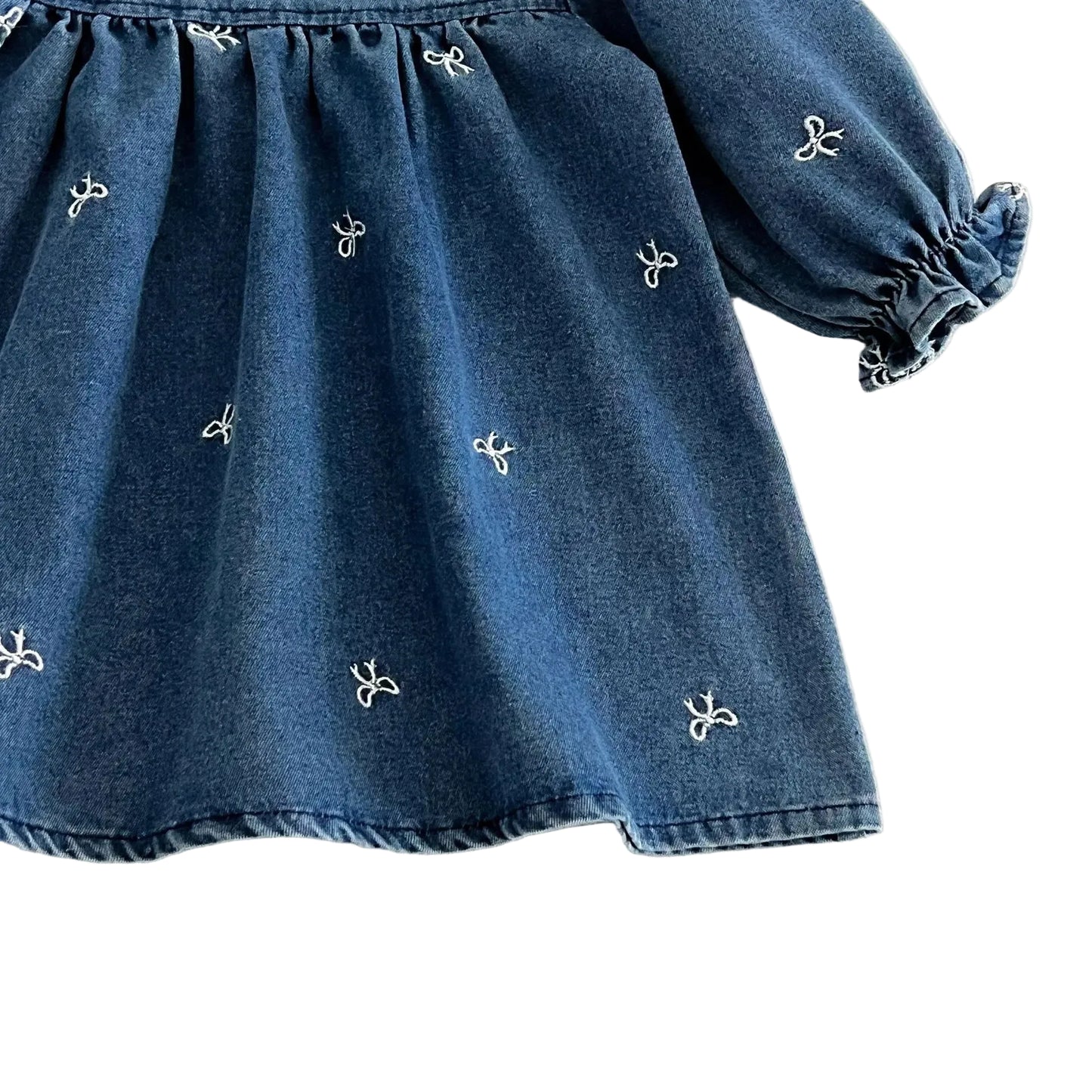 Close up of the blue denim twill fabric showing the delicate white embroidered bows and the flowing drape of the skirt.