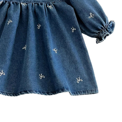 Close up of the blue denim twill fabric showing the delicate white embroidered bows and the flowing drape of the skirt.