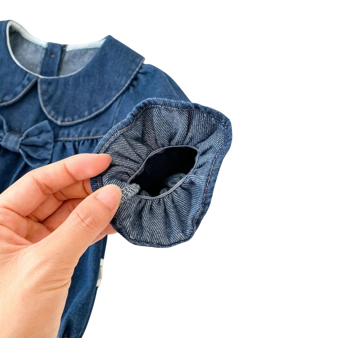 Hand demonstrating soft elastic stretch of ruffle sleeve cuff on baby denim bubble romper