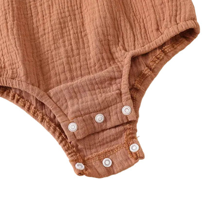 Open view of the inner reinforced seam stitching around the bottom metal diaper snaps on a premium cotton muslin infant onesie.