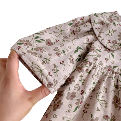 Hand holding the gently gathered elastic wrist cuff of the long-sleeve floral baby romper to show stretch and comfortable fit.