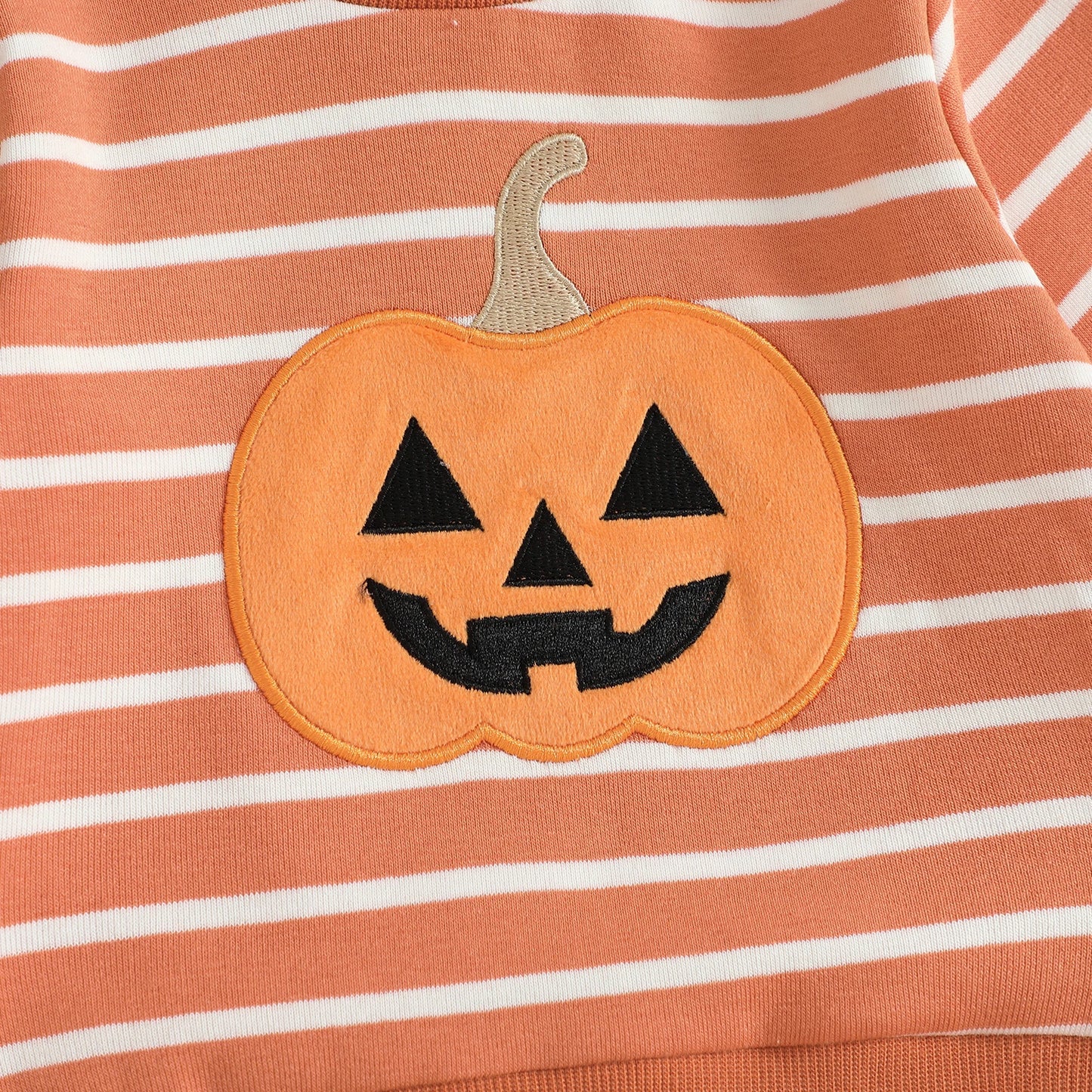 Close-up detail of the high-quality embroidered smiling jack-o'-lantern pumpkin patch on the chest of the orange and white striped toddler sweatshirt.