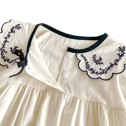 Close-up of the ivory scalloped lapel collar featuring detailed floral embroidery and a small delicate center bow.