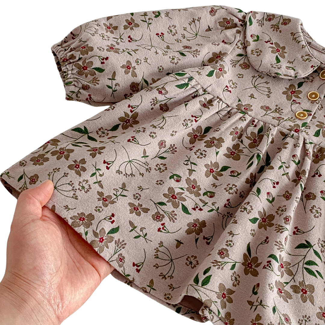 Close-up of a hand holding the flared skirt of the Kidsely floral dress, highlighting the earthy botanical print and soft cotton-blend fabric.