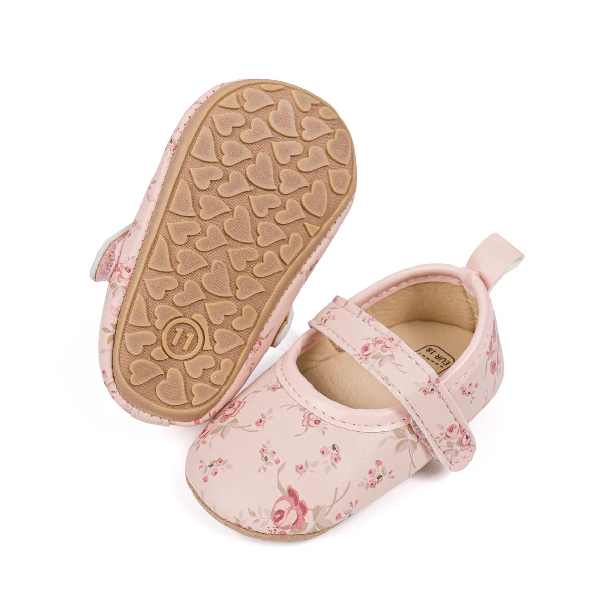 Pink floral baby shoe next to an upturned shoe displaying the flexible brown rubber sole with heart grips.