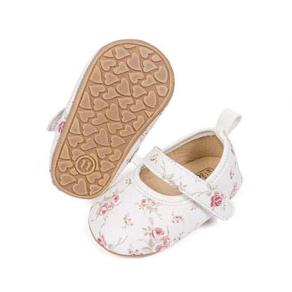 White floral baby shoe next to an upturned shoe displaying the flexible rubber heart-shaped traction grips.