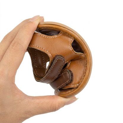 Hand bending a brown baby sandal in half to demonstrate the ultra-flexible soft sole.