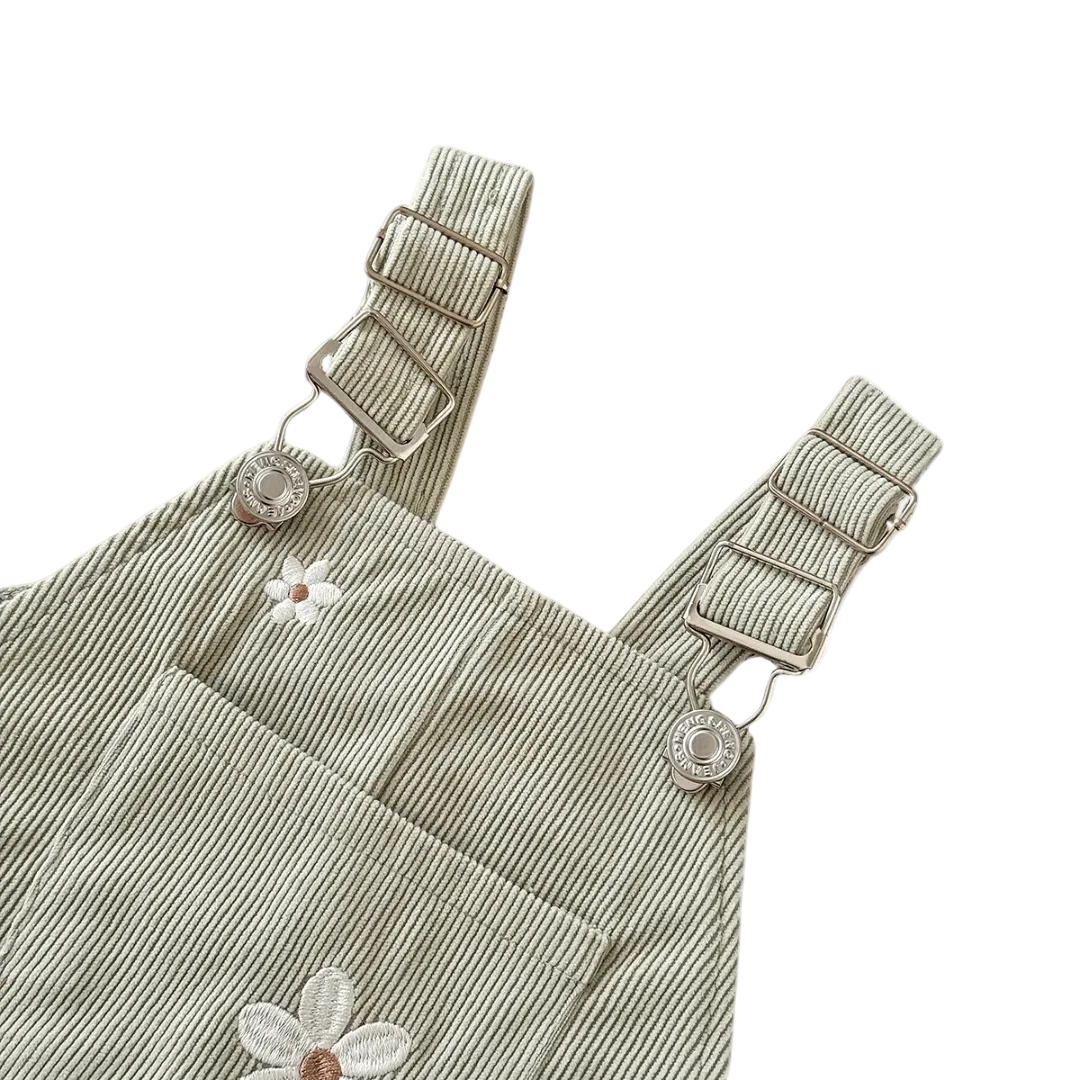 Close-up of the front pocket and adjustable metal buckle straps on the Sage Green floral baby overalls.