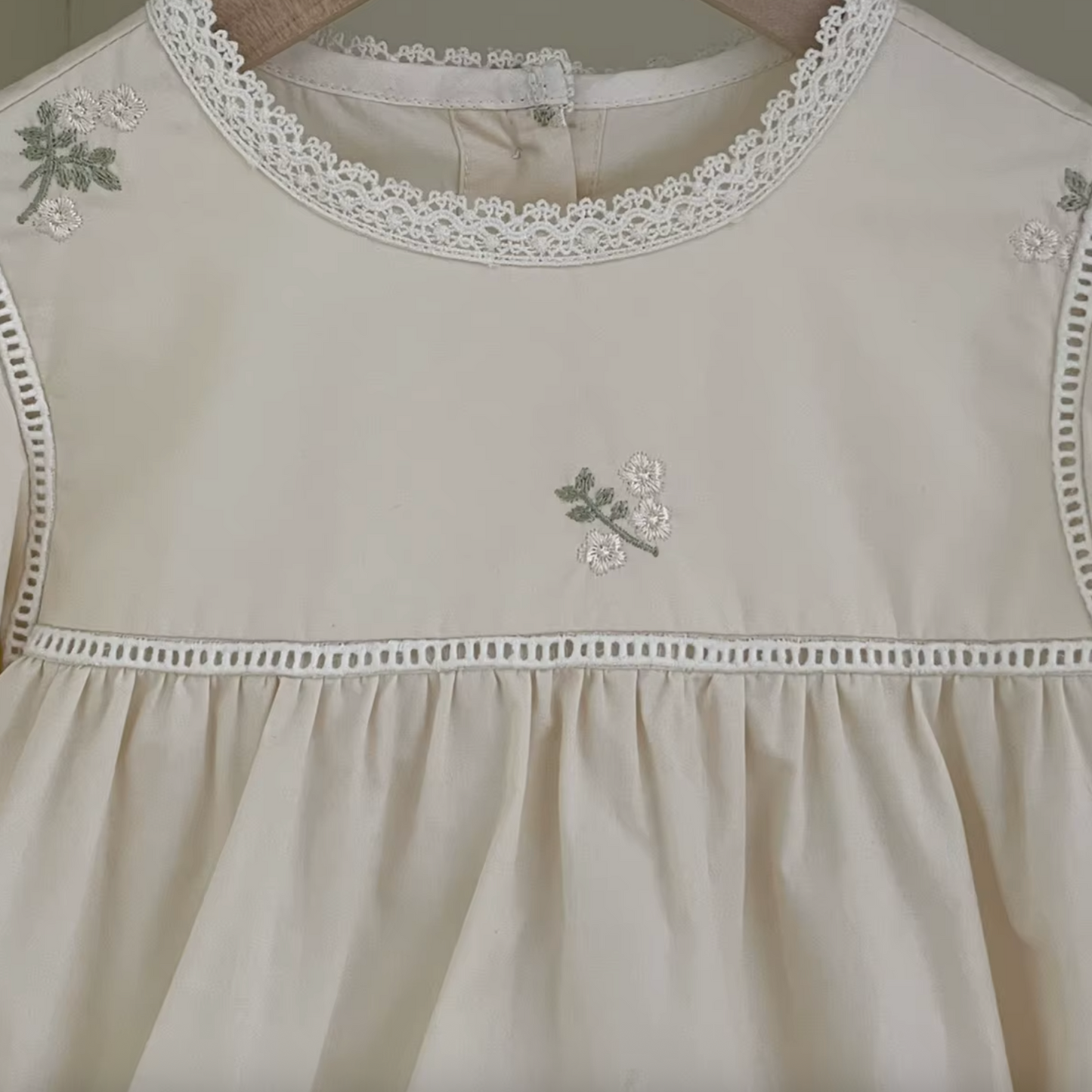 Close-up shot of cream cotton fabric showing delicate floral embroidery and lace trim on chest and neckline