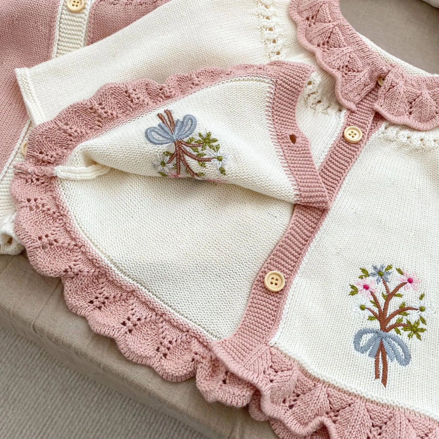 Close-up detail of hand-stitched floral embroidery and wooden buttons on a cottagecore baby knit cardigan sweater.