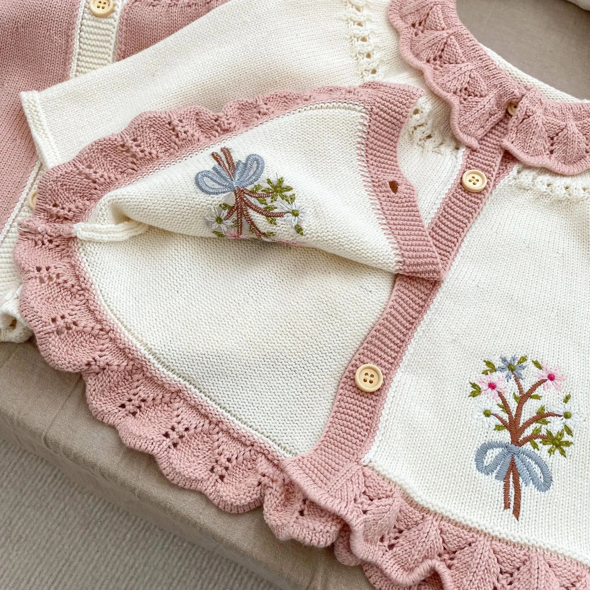 Close-up detail of hand-stitched floral embroidery and wooden buttons on a cottagecore baby knit cardigan sweater.