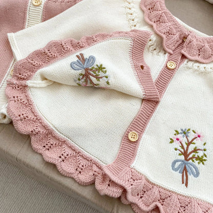 Close-up detail of hand-stitched floral embroidery and wooden buttons on a cottagecore baby knit cardigan sweater.