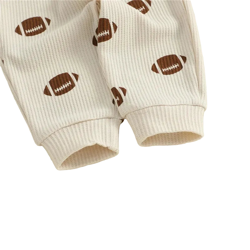 Close-up of the ribbed ankle cuffs on the beige toddler jogger pants featuring a repeating brown football pattern.