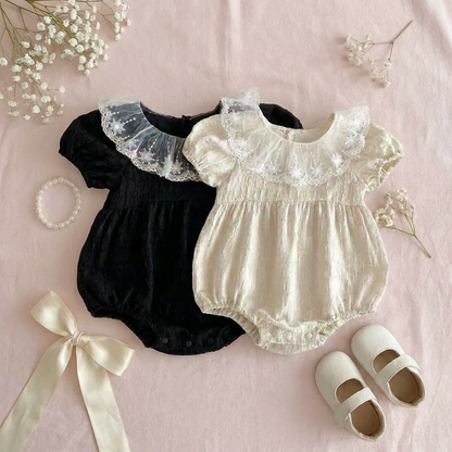 Two baby rompers, a pair of shoes, and a ribbon on a pink background with baby's breath flowers.