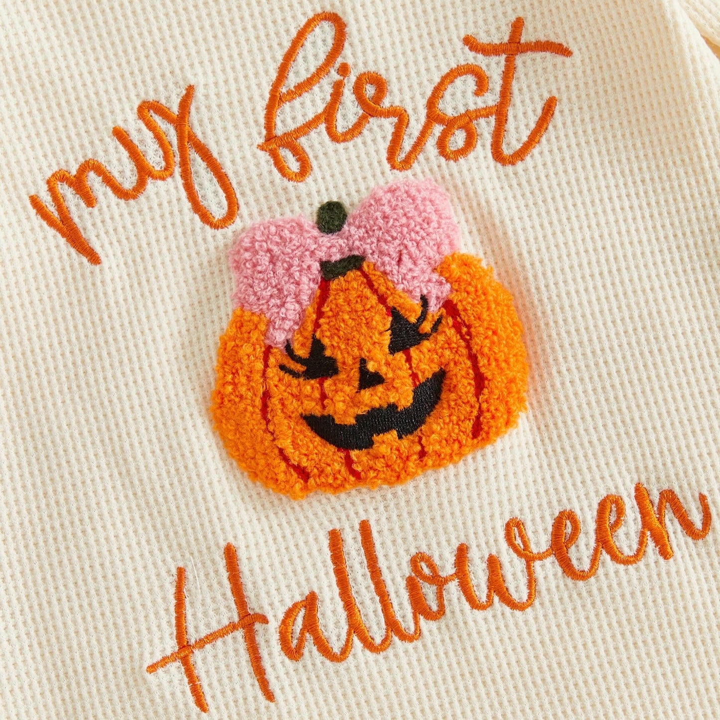 Close-up of the textured fuzzy orange pumpkin appliqué with a pink bow and "My first Halloween" embroidery on a ribbed baby romper.