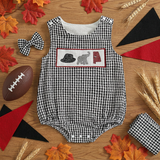 Flat lay view of the black and white seersucker smocked elephant baby romper arranged on a wooden surface with decorative autumn leaves, a mini football, a matching bow tie, and fabric pennants.