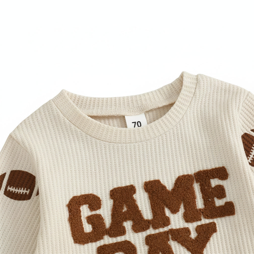 Close-up of the round neckline and partial "Game Day" brown embroidery on the beige waffle-knit toddler sweater.