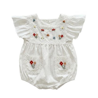Flat lay of a white eyelet baby romper with Garden Floral embroidery, flutter sleeves, and daisy lace trim on a white background.