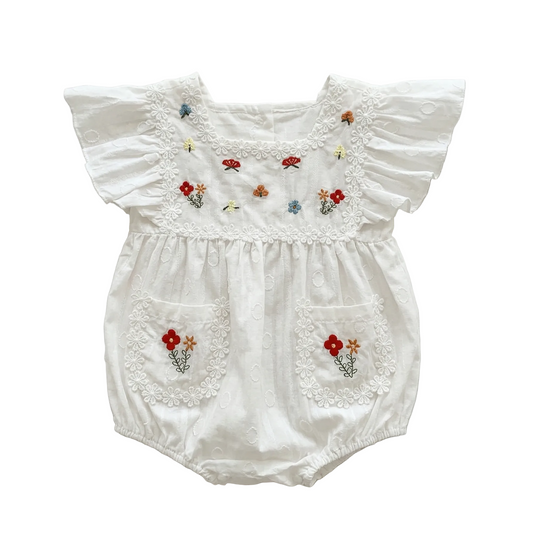 Flat lay of a white eyelet baby romper with Garden Floral embroidery, flutter sleeves, and daisy lace trim on a white background.