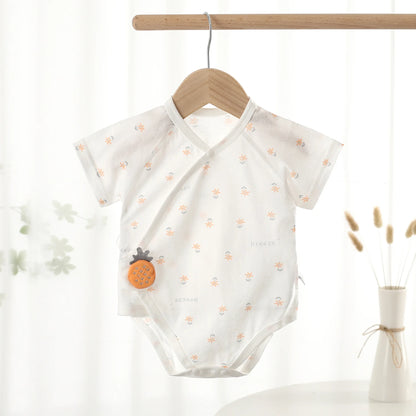 Gender-neutral white floral breeze print baby bodysuit featuring a plush orange pineapple detail, hanging elegantly on a wooden clothing rack.