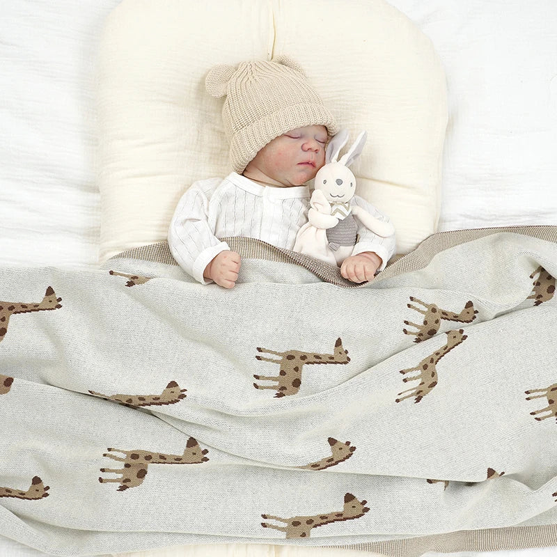 Peaceful infant sleeping comfortably tucked under the cozy giraffe knit baby blanket