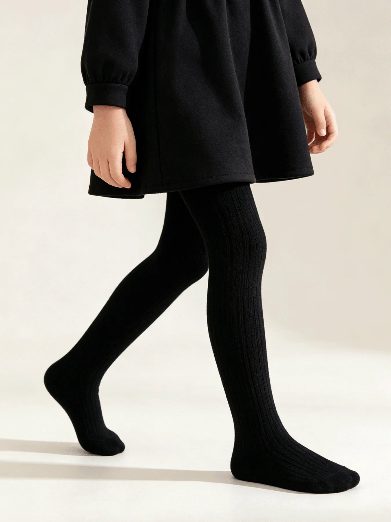Little girl modeling opaque black cable knit tights layered under a dark dress.